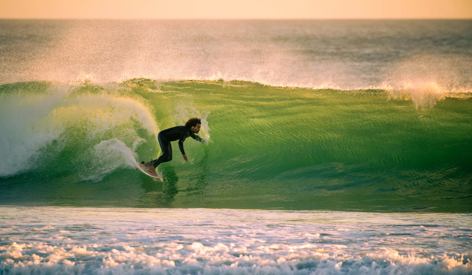 A surfer carving inside a green, golden-hour wave